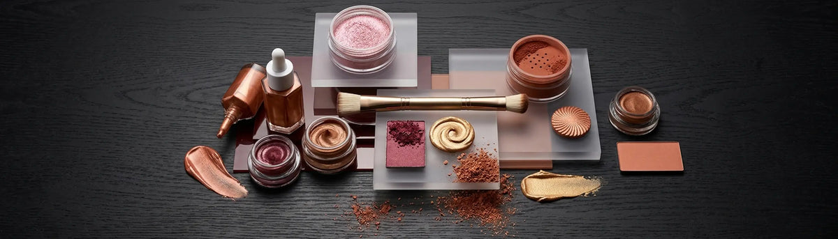 Various cosmetic products and PVD optical pigment powders arranged on a dark tabletop, viewed from above